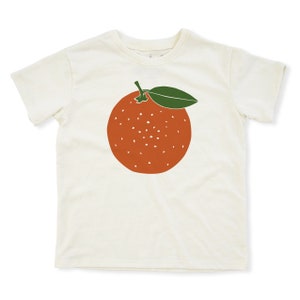 May include: A white t-shirt with a graphic of an orange with a green leaf on the front.