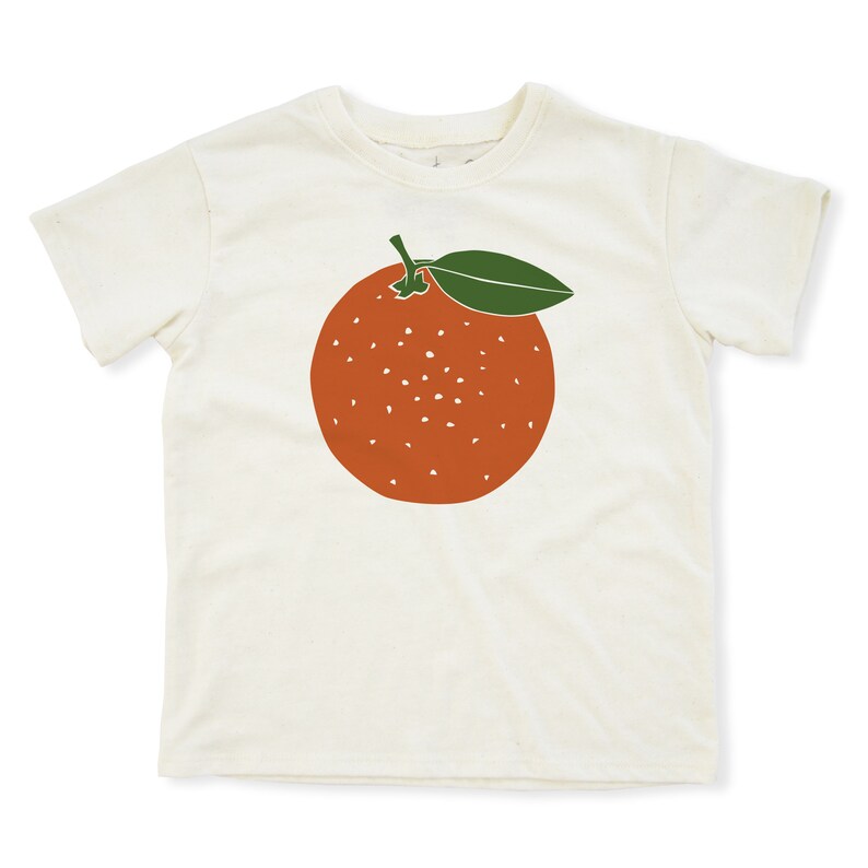 May include: A white t-shirt with a graphic of an orange with a green leaf on the front.