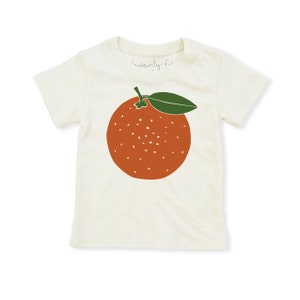 May include: A white t-shirt with a green leaf and orange fruit graphic. The text "twenty-five" is printed on the shirt.