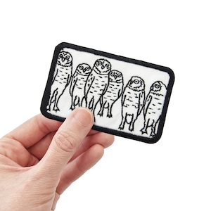 May include: Black and white embroidered patch featuring a row of six owls with black eyes and beaks. The owls are standing upright with their wings tucked in. The patch is rectangular and has a black border.