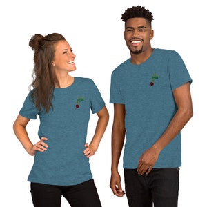 May include: Two people wearing blue heather t-shirts with a small embroidered image of a beet on the left chest. The beet is red with green leaves.