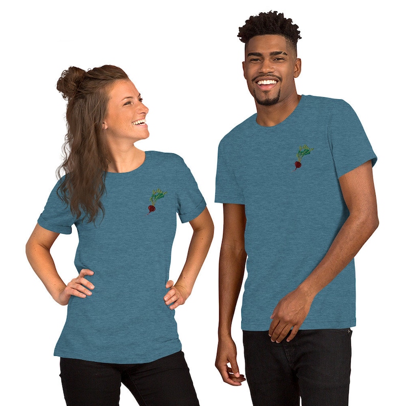May include: Two people wearing blue heather t-shirts with a small embroidered image of a beet on the left chest. The beet is red with green leaves.