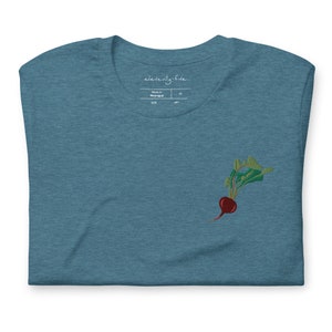 May include: A teal blue t-shirt with an embroidered beet design. The shirt has a tag that says "eleventy-five" and "Made in Nicaragua".