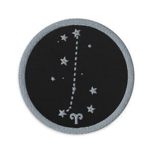 May include: A black and silver embroidered patch with the constellation Aries, a ram's head, and the text "Aries".