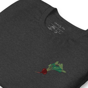 May include: Dark heather grey t-shirt with an embroidered image of a red beet with green leaves. The shirt has a tag that says "eleventy-five" and includes the size and material composition.