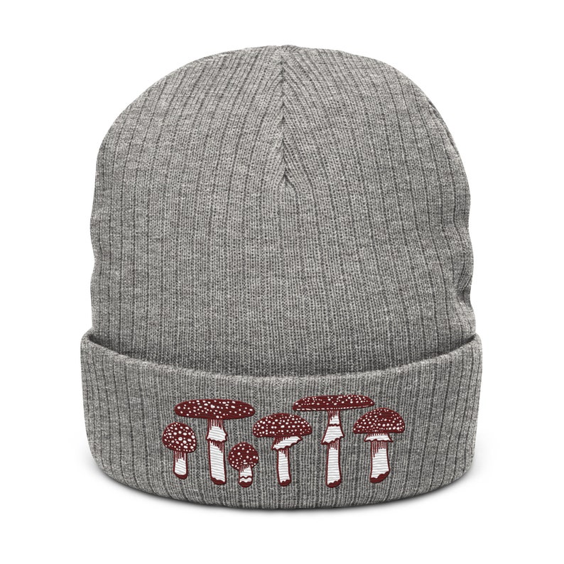 May include: Gray knitted beanie with a red and white mushroom design. The mushrooms are arranged in a row across the bottom of the beanie.