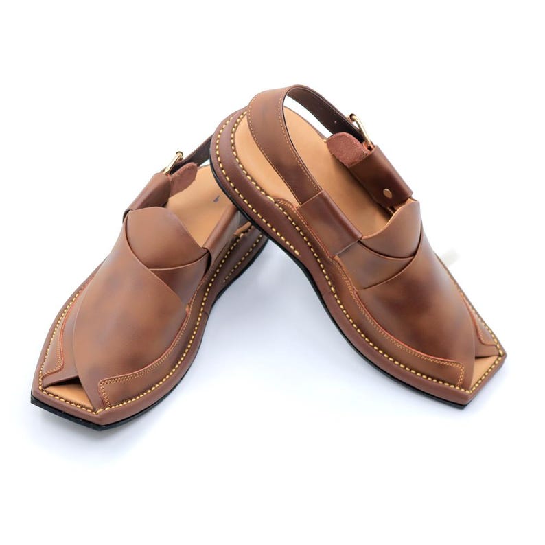 May include: A pair of brown leather sandals with a buckle strap and a pointed toe. The sandals have a stitched design around the edge of the sole.