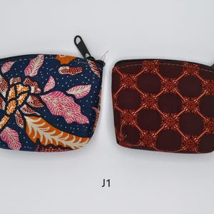 Op de afbeelding: Twee kleine etuis met ritssluiting. Eén is marineblauw met een bloemenpatroon in oranje en roze. De andere is bordeauxrood met een herhalend geometrisch ontwerp in oranje. Beide hebben zwarte ritsen en trektouwtjes. De etuis staan op een witte achtergrond.