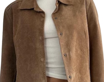 May include: A brown suede jacket with a collared neckline and button-down front. The jacket is a warm, earthy tone and appears to be a vintage or retro style. The jacket is worn over a white top.