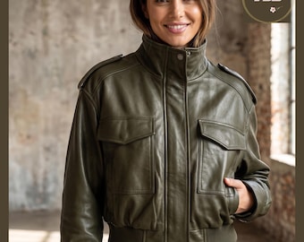 May include: Olive green leather jacket with a high collar, two front pockets, and a ribbed hem. The jacket has a button closure and shoulder epaulets. The jacket is a bomber style.