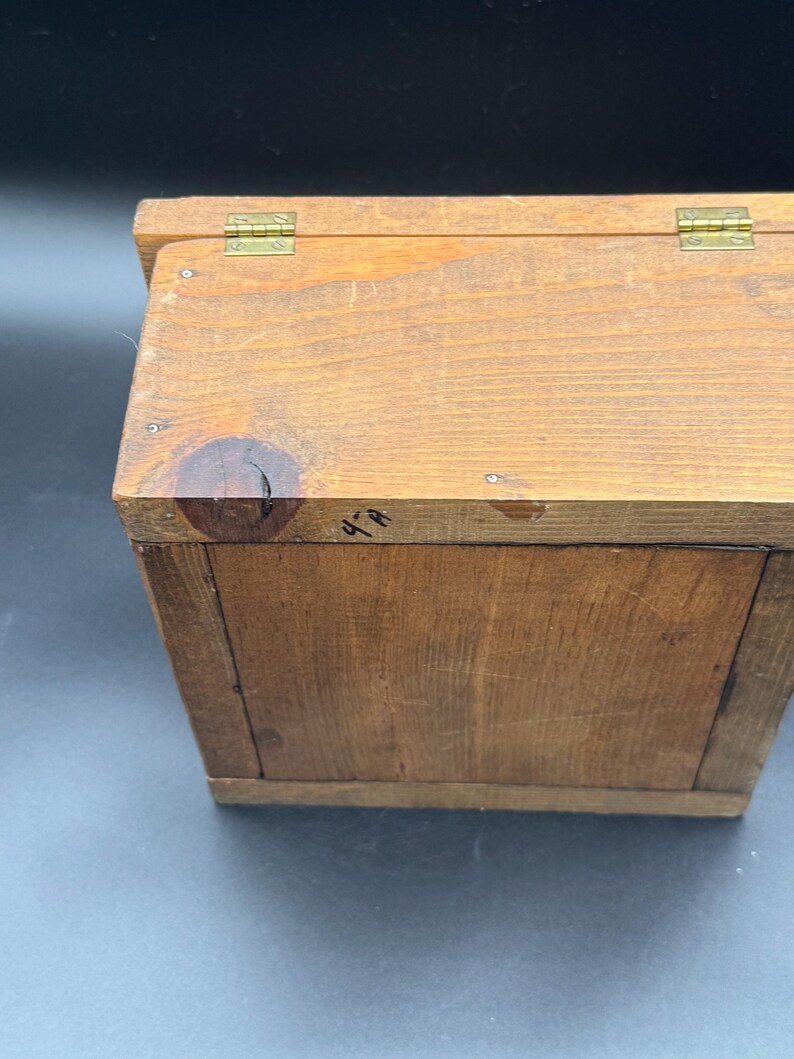 May include: A small, handcrafted wooden box with a hinged lid. The box is made of light brown wood and features brass hinges. The wood grain is visible, and the box appears to be well-constructed. The box is likely used for storage.