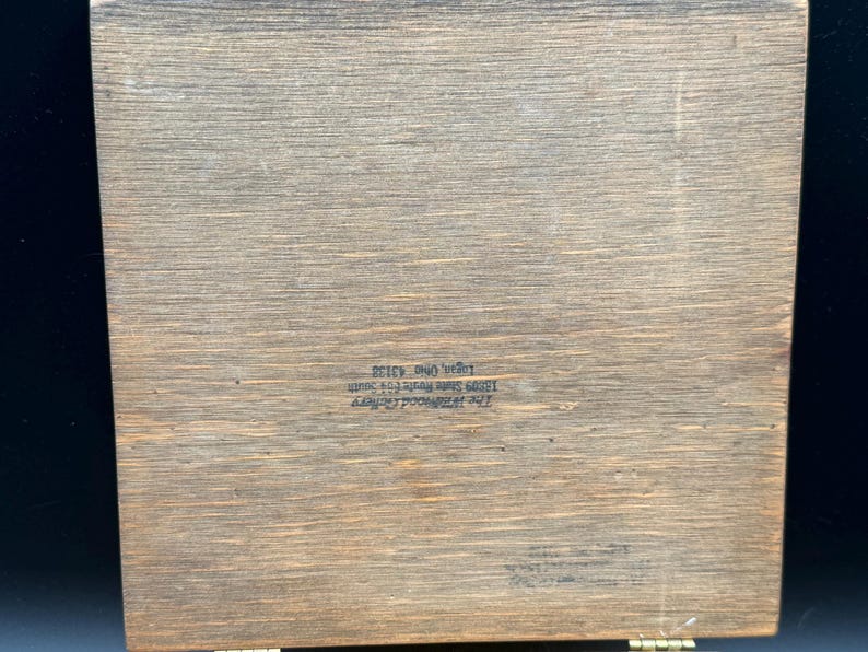May include: A rectangular wooden box with a hinged lid. The wood has a natural grain pattern and a warm, brown tone. Text is printed on the wood. The box appears to be vintage or antique.