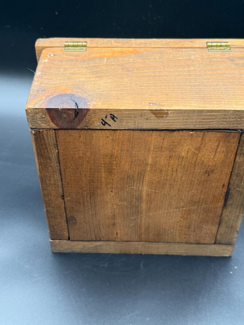 May include: A small, rectangular wooden box with a hinged lid. The box is constructed from light brown wood and features visible wood grain. The lid is attached with brass hinges. The text "4-A" is written on the side of the box.