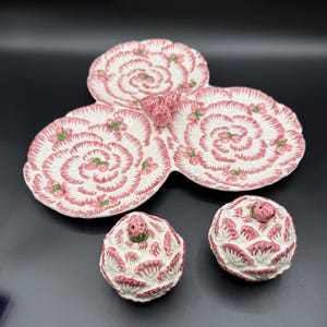 May include: A white ceramic serving dish with three sections and two matching lidded containers. The dish and containers feature a pink and white strawberry design with green accents. The set is ideal for serving snacks or desserts.