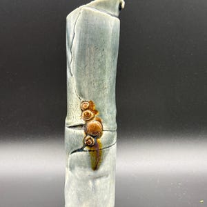 May include: A tall, cylindrical ceramic vase with a glossy, mottled blue-gray glaze. The surface features a prominent vertical crack and a cluster of raised, circular, brown-glazed decorative elements that resemble small shells or buttons.