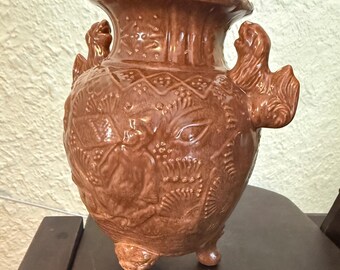 Brown-glazed ceramic urn vase featuring molded relief decorations, decorative stylized handles, and a tripod claw-foot base