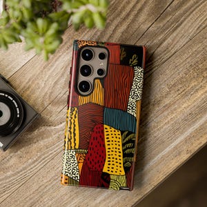 May include: A patterned phone case with a patchwork design. The case features a variety of colours, including red, yellow, brown, and black. The case has a glossy finish and is designed for a smartphone with multiple camera lenses.