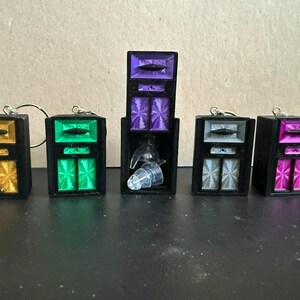 May include: Five rectangular black cases with metallic-coloured inserts in gold, green, purple, silver, and pink. Each case features a top compartment with a horizontal bar and a lower section with two vertical panels. One case is open, revealing earplugs.