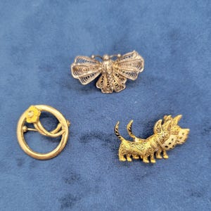 May include: Three silver and gold brooches. One is a delicate butterfly design, another is a circle with a yellow flower, and the third is a stylized dog.