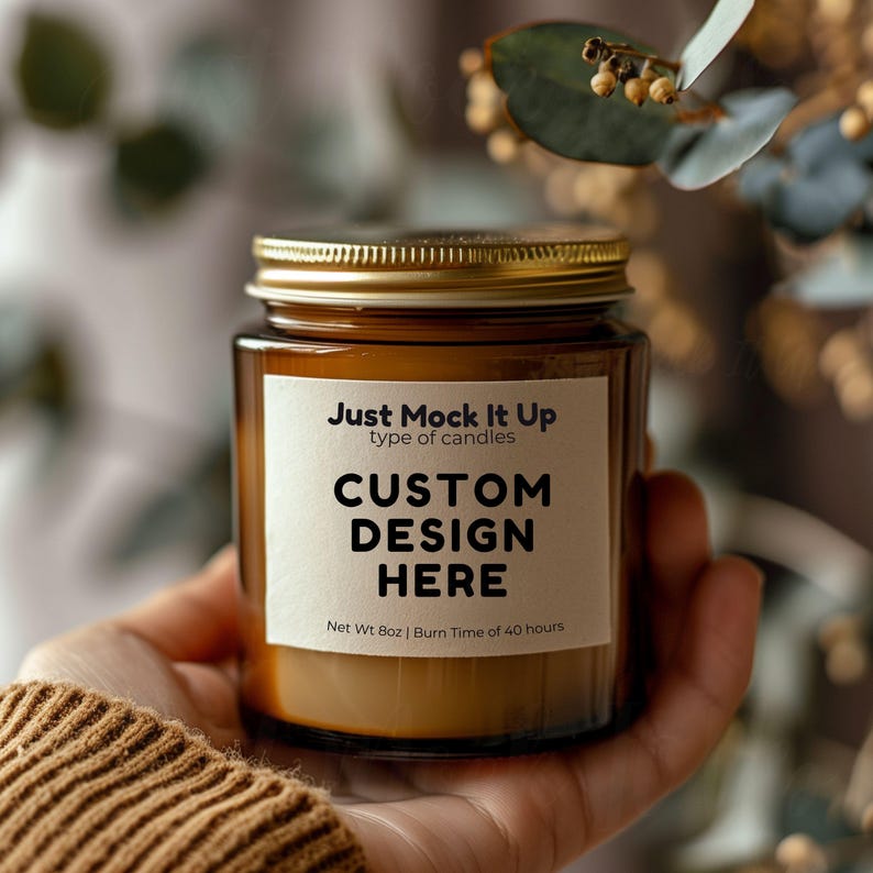 May include: A brown glass candle jar with a gold lid. The label reads "Just Mock It Up type of candles CUSTOM DESIGN HERE Net Wt 8oz | Burn Time of 40 hours".