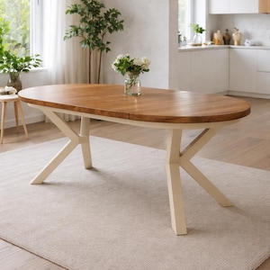 Peut inclure: Une table de salle à manger ovale en bois avec un plateau marron clair et des pieds blanc cassé. La table est posée sur un tapis beige clair dans une pièce lumineuse avec une fenêtre et un vase de fleurs blanches. La table mesure environ 183 cm de long.