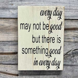 May include: White wooden sign with black text that reads "every day may not be good but there is something good in every day".