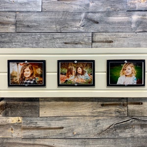 May include: Three black picture frames with white mats, each containing a photograph of a young girl. The frames are mounted on a white wooden board.