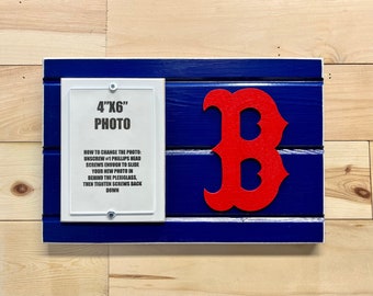 May include: A blue and white wooden sign with a red "B" in the center. The sign has a white frame with a 4"x6" photo insert. The sign includes instructions on how to change the photo.