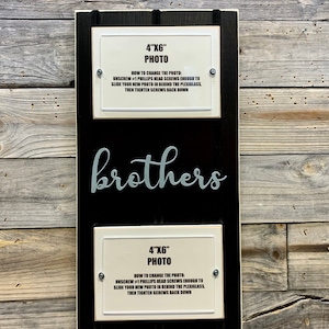 May include: A black wooden frame with two white 4x6 inch photo frames. The frames have instructions on how to change the photos. The word "brothers" is written in gray cursive letters on the frame.