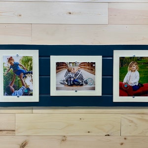 May include: A navy blue picture frame with three white mats and three photos of children. The photos are of a girl being held up by a man, two children sitting on a bridge, and a girl sitting on a red cushion.