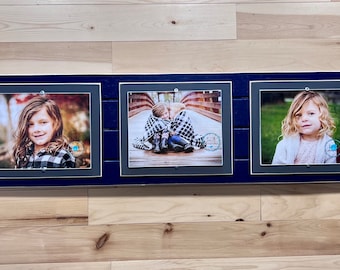 May include: Three framed photographs on a wood wall. The frames are navy blue with a silver trim. The photos are of children. The first photo is of a girl with long brown hair wearing a black and white plaid shirt. The second photo is of two children sitting on a wooden bridge. The third photo is of a girl with long blonde hair wearing a white shirt.