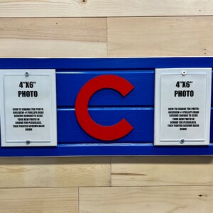 May include: A blue and white wooden sign with a red "C" in the center. The sign has two white frames with the text "4"x"6" Photo" and instructions on how to change the photo.