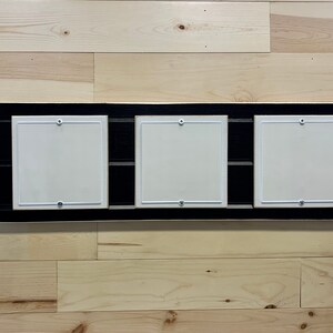 May include: Three black picture frames with white mats and silver mounting hardware are mounted on a light wood wall.