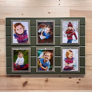 May include: A six-photo collage frame with a dark green painted wooden frame. Each photo is held in place with a silver metal clip. The photos feature a young girl in various settings.