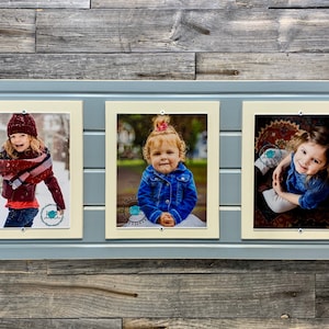 May include: A triple photo frame with three individual picture openings. The frame is light blue with a wooden plank design. Each opening contains a photograph of a child. The background is a weathered wood.