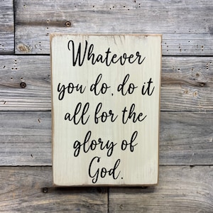 May include: White wooden sign with black text that reads "Whatever you do, do it all for the glory of God."