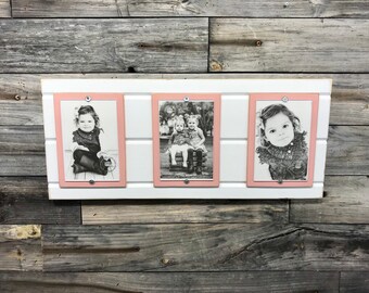 May include: Three black and white photos of children are displayed in a white picture frame with pink trim. The frame is mounted on a wood wall.