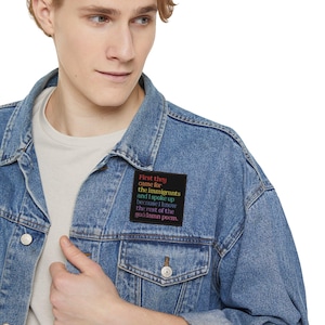 Può includere: Giacca di jeans blu chiaro con una toppa nera. La toppa presenta testo in rosso, giallo, verde e viola. Il testo recita: "First they came for the immigrants and I spoke up because I know the rest of the goddamn poem."