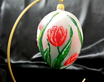 Glazen, handbeschilderd paasei met rode tulpen op een matte witte achtergrond, lenteversiering.