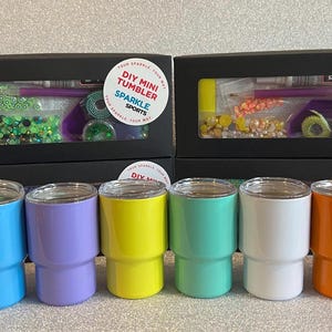 Może przedstawiać: Kolekcja kolorowych mini kubków w kolorach zielonym, niebieskim, fioletowym, żółtym, turkusowym, białym, pomarańczowym i różowym. Każdy kubek ma srebrną obręcz. Zestawy mini kubków DIY z napisem "DIY MINI TUMBLER SPARKLE SPORTS" są widoczne.