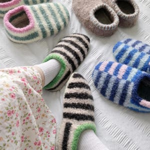 以下が含まれることがあります： カラフルなウールフェルトのスリッパの数々。白黒、青とピンク、緑と白のストライプ模様など、いくつかのペアが見えます。スリッパは柔らかく快適で、室内履きに最適です。