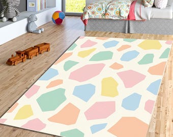 May include: A rectangular area rug with a cream-colored background and colorful, irregular geometric shapes in pastel shades of pink, blue, yellow, green, and orange. The rug is placed on a wooden floor.