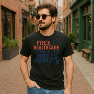May include: Black t-shirt with the text "FREE HEALTHCARE FOR A FREE PEOPLE" in red and blue. A blue stethoscope graphic is also featured. The shirt is being worn outdoors.
