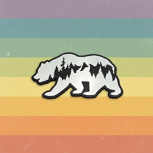 May include: A white bear-shaped sticker with a black outline. The bear's silhouette features a mountain and forest design. The background is a rainbow gradient.