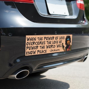 Op de afbeelding: Een rechthoekige bumpersticker met de quote "WHEN THE POWER OF LOVE OVERCOMES THE LOVE OF POWER THE WORLD WILL KNOW PEACE - Jimi Hendrix." De sticker heeft een portret van Jimi Hendrix.