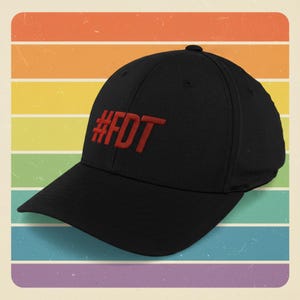 Può includere: Cappellino da baseball nero con la scritta rossa ricamata "#FDT". Il cappellino è posto su uno sfondo di strisce orizzontali dai colori dell'arcobaleno.