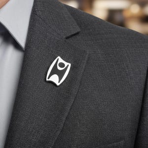 May include: A black and white enamel pin with a stylized human figure design. The pin is attached to a dark gray suit jacket. The pin has a white border and a black interior.