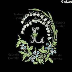 May include: Embroidered design of the letter L surrounded by white lily of the valley flowers and blue forget-me-not flowers. The letter is in a silver colour and the flowers are green and white.