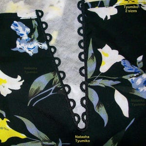 May include: Close-up of a black fabric with a floral print in shades of yellow, white, and blue. The fabric has a black lace trim along the neckline. The text "Natasha Tyumiko" is printed on the fabric.