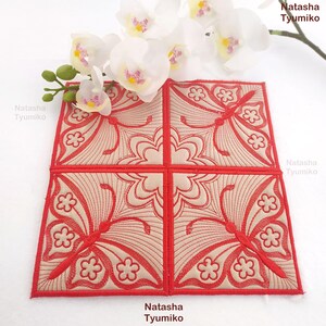 May include: A square, quilted coaster set featuring a repeating butterfly and floral design in red and beige. The coaster set is made of four individual squares, each with a detailed embroidered pattern. White orchids are in the background.